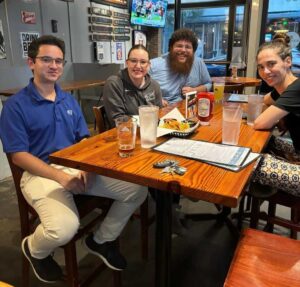 Four young adults have drinks at a table.