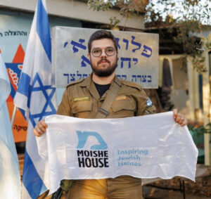 Male IDF soldier standing with Moishe House flag